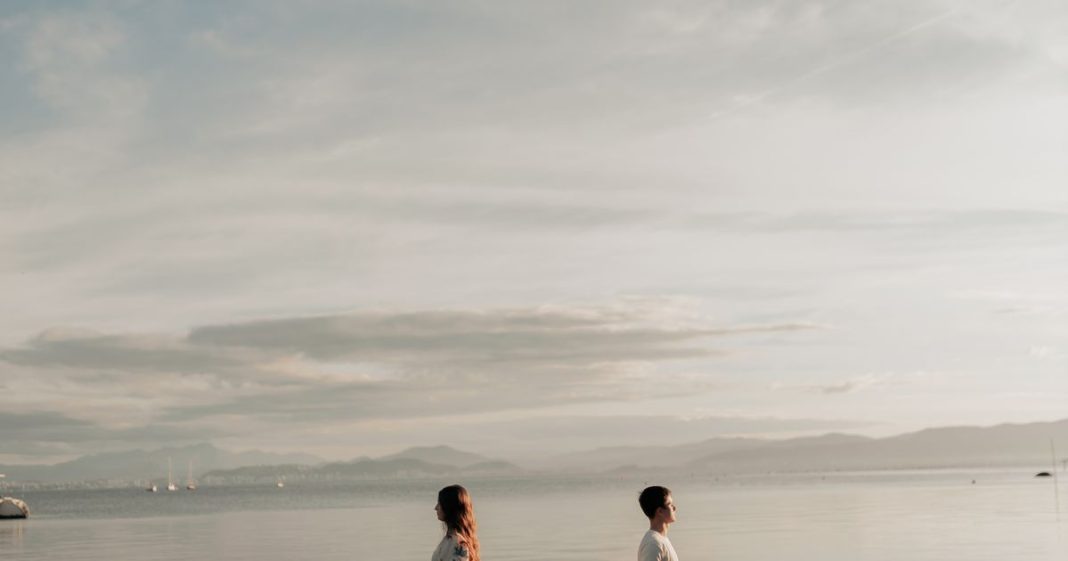 Couple standing apart on a beach at sunset